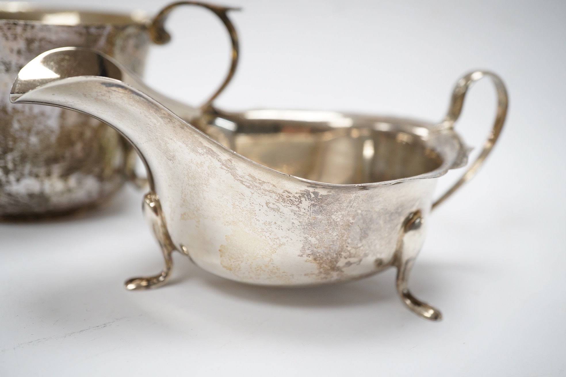 A George III Scottish silver cream jug, later embossed, a pair of George V silver sauce boats and an Edwardian hammered silver two handled porringer, by Moss Morris,18.4oz. Condition - poor to fair